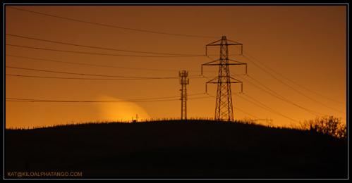 Pylons at Night: Two pylons at night with the light behind them.  One is an electrical pylon, the other I believe, is a radio mast.